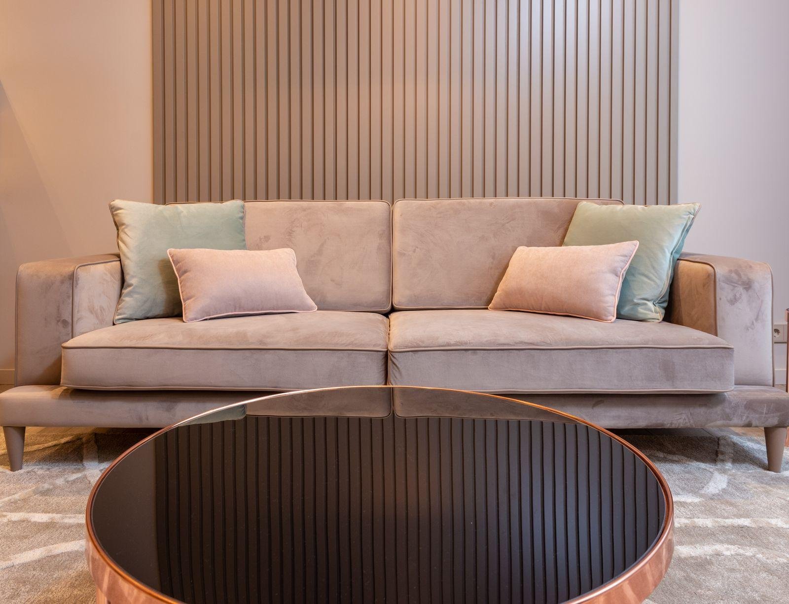 Beige velvet sofa with pastel cushions against a timber slat wall – reupholstery ideas for Auckland living rooms