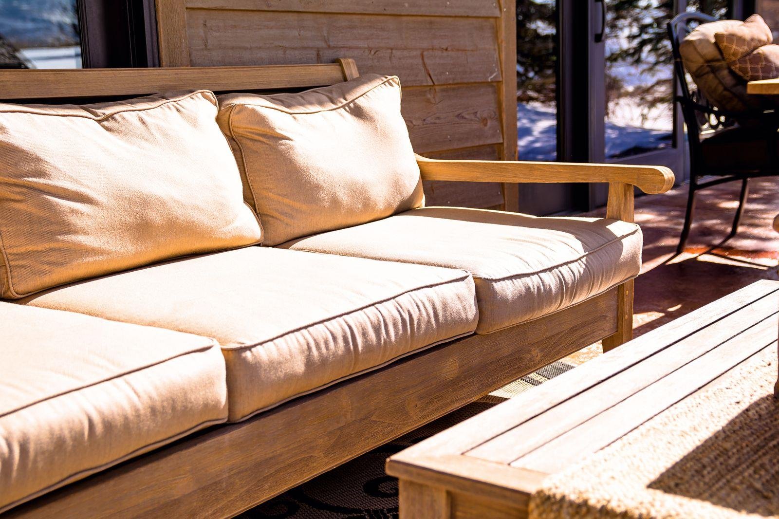 Timber outdoor sofa with thick cream cushions on a sunny deck – outdoor furniture reupholstery in Auckland