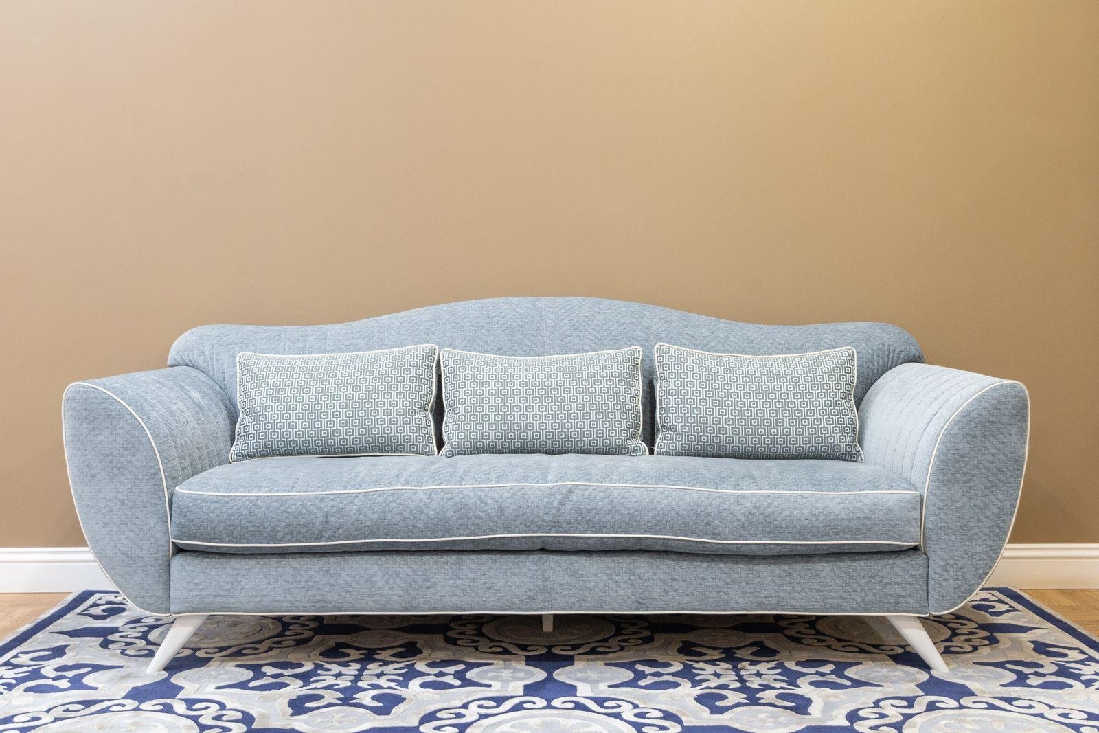 Light blue two-seater sofa on a patterned rug against a plain wall – sofa reupholstery costs in Auckland