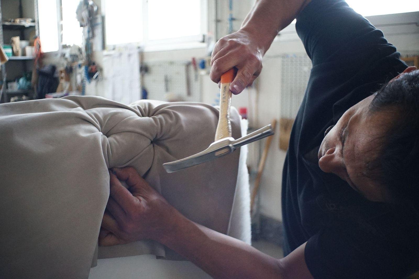 Upholsterer tacking new fabric onto a sofa cushion with a magnetic hammer in a workshop