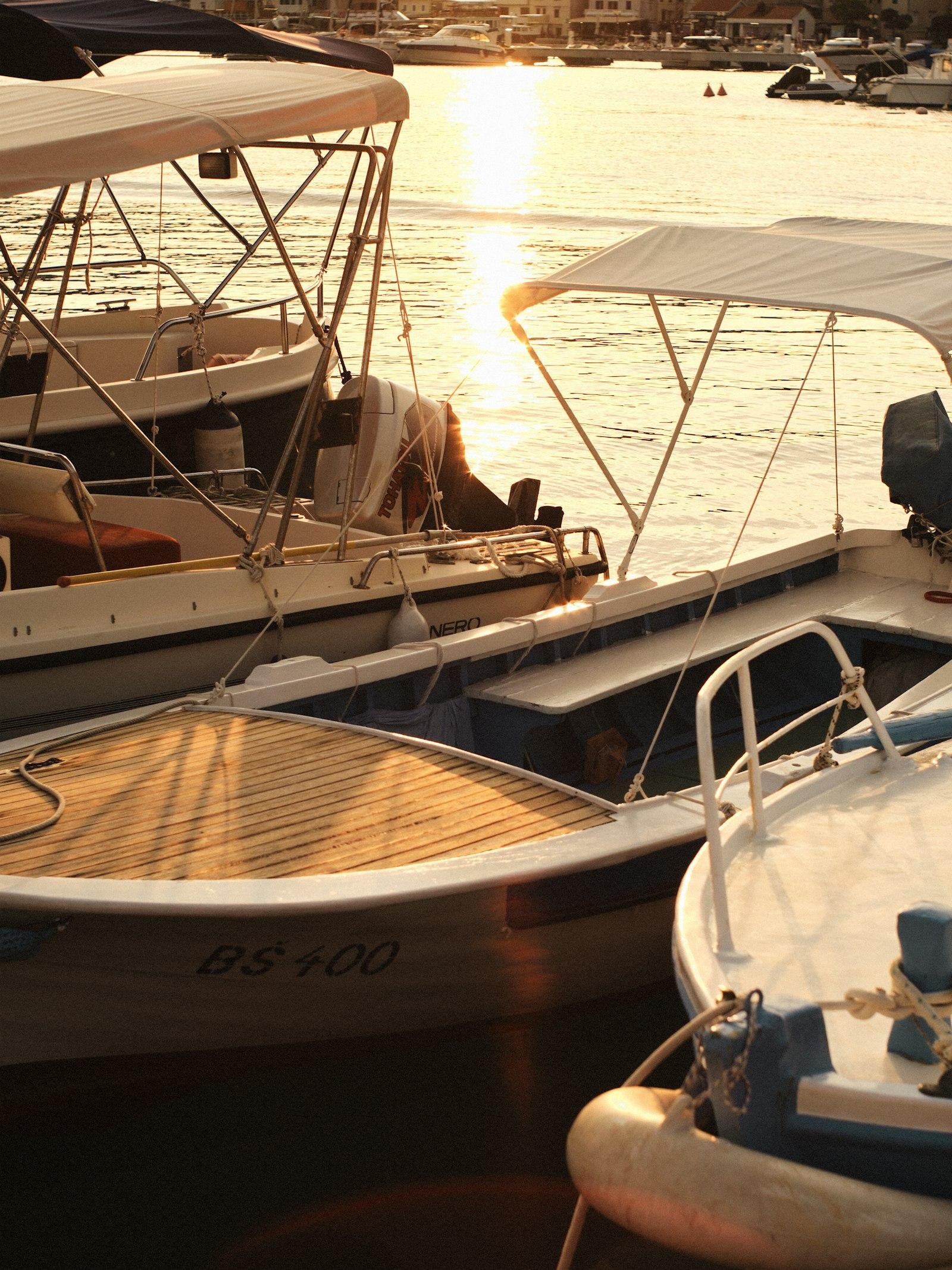 Motorboats with bimini tops tied up side by side on marina berths in low evening sun