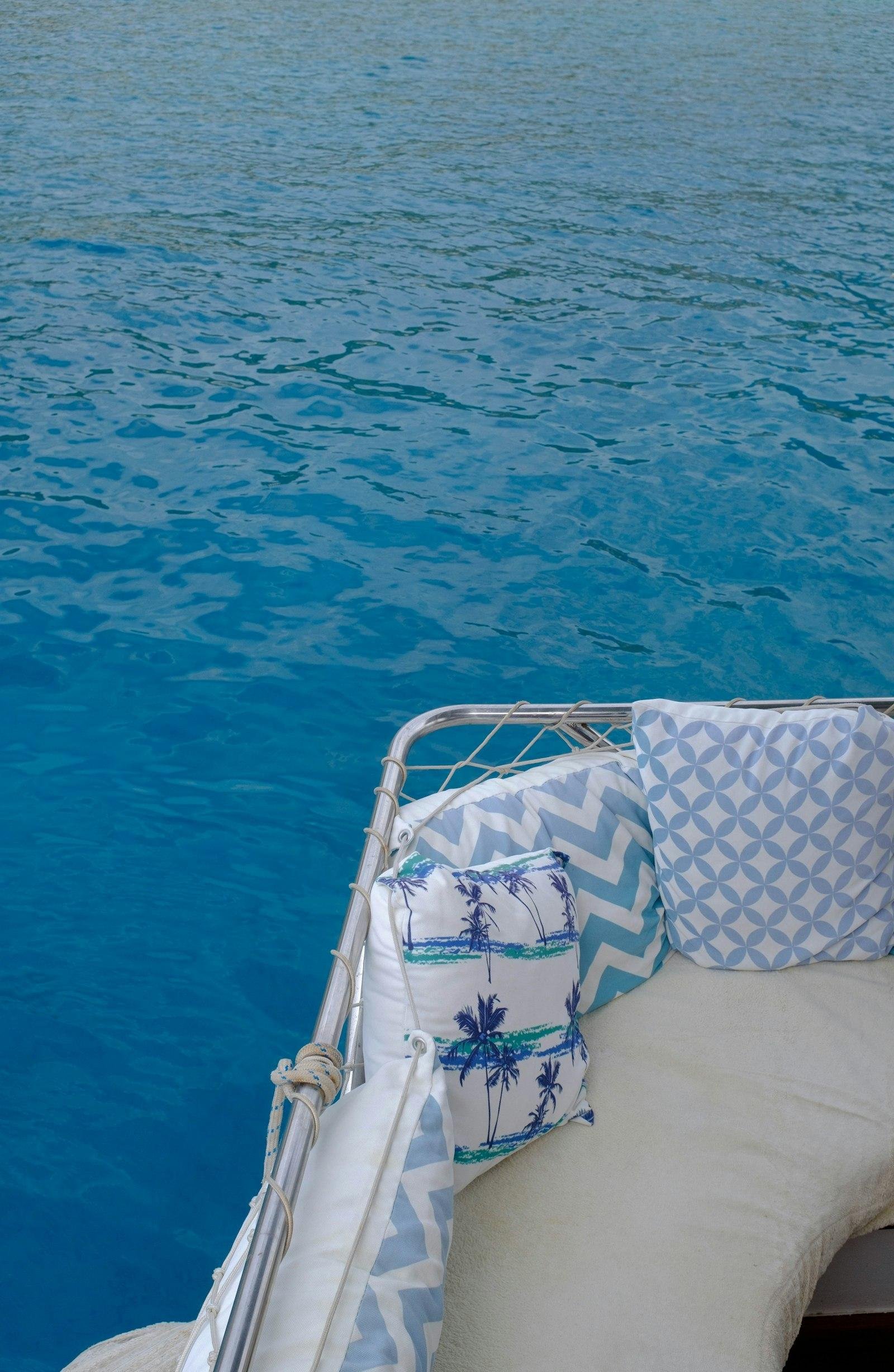 Blue and white patterned cushions on a boat deck in bright sun above clear blue water