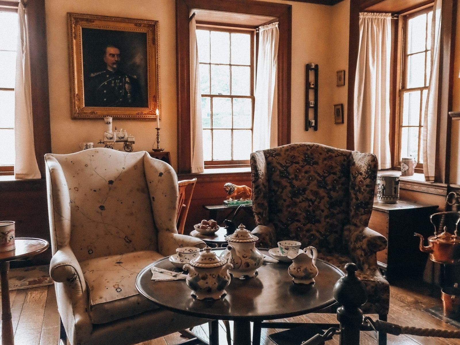 Two patterned wingback armchairs around a small table with a tea set in a period-style room with sash windows